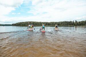 Paddleboarders on a Calm Lake with Forested Shoreline and Clouds photo