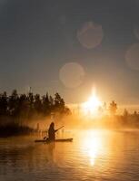 Person Paddling on Calm Water at Sunrise with Mist and Trees photo