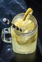 Glass Mason Jar of Lemonade with Ice and Lemon Garnish on Dark Surface photo
