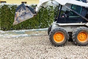 Skid Steer Loader with Orange Wheels on Crushed Stone Surface photo