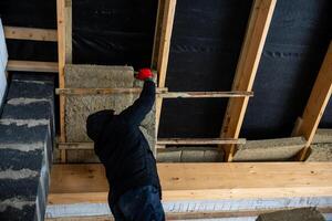 Worker Installing Insulation in Partially Constructed Building Frame photo
