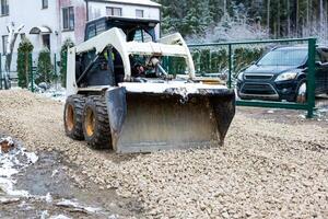 Skid Steer Loader Spreading Gravel at a Snowy Construction Site photo