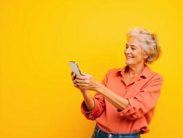 Joyful Senior Woman Engaged with Smartphone against a Bright Yellow Background photo