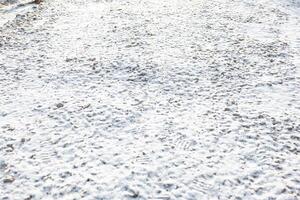 Snow Covered Ground with Footprints and Scattered Pebbles photo