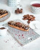 Chocolate Eclair with Nuts on Patterned Board and Tea Setup photo