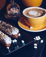 Close Up of Latte with Leaf Foam Design and Eclairs on a Table photo