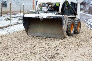 Skid Steer Loader Spreading Gravel on Snow Dusted Pathway photo
