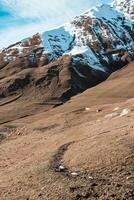Snow Capped Mountain with Dry Terrain and Winding Path in Georgia photo