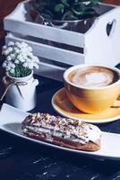 Yellow Coffee Cup with Latte Art and Eclair on Dark Tabletop photo