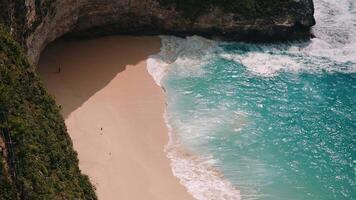 Person walking to ocean waves on Kelingking Beach with cliffs video