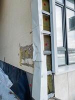 There is noticeable exterior damage on the wall of the building located near a window, which has resulted in insulation being exposed and visible to the outside elements photo