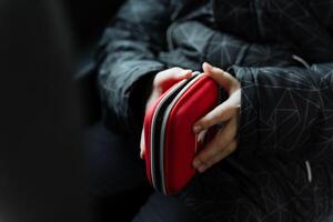 A person is confidently holding a stylish red case in their hands, likely made of leather, which may contain various gadgets or essentials for their everyday carry needs photo