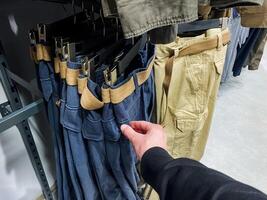 A person is currently in a clothing store selecting a stylish pair of pants, examining various options available, which may include denim fabrics and functional details like pockets photo
