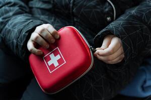 A person is currently holding a vibrant red first aid kit that has a prominent white cross symbol on it, indicating its purpose and contents clearly for emergency situations photo