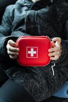 A person is firmly holding a vibrant red first aid kit in their hands, ready to address any potential medical emergencies that may arise during their activities or travels photo