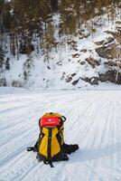 A vibrant yellow and red backpack is resting quietly in the soft, white snow, creating a contrast that catches the eye and brings a sense of adventure to the winter landscape photo