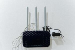 A wireless router is placed on a clean white wall right next to an electrical charger, which is also an essential electronic device for powering various gadgets and technology photo