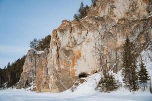 The snowcovered rock formation has inviting entrances, surrounded by tall evergreens, creating a serene winter landscape that evokes tranquility and adventure photo