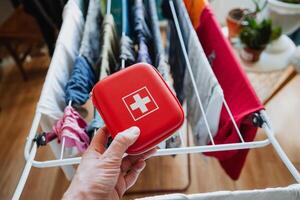 Having a First Aid Kit readily available in hand along with clothes drying on a rack signifies essential home safety measures for maintaining health and wellness practices photo