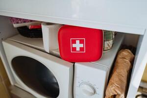 A red First Aid Kit positioned conveniently on top of the washing machine, easily accessible for home storage in case of any emergency health situations that may arise photo