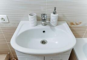 The bathroom sink features a toilet brush and a soap dispenser conveniently placed on its surface, contributing to the cleanliness and functionality of this essential plumbing fixture in the bathroom photo