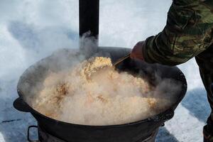 A person is actively stirring a pot filled with food while surrounded by snow, creating a cozy and warm scene in a wintery outdoor environment, despite the cold weather conditions photo
