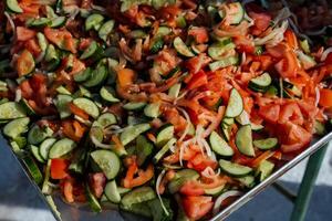 A large metal tray that is filled with fresh tomatoes, crisp cucumbers, and pungent onions, creating a vibrant assortment of ingredients perfect for salads and various dishes photo
