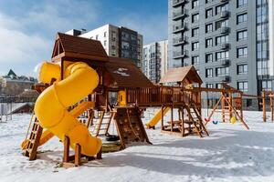A delightful childrens playground covered in a blanket of snow, featuring various play structures, with a building in the background adding to the winter wonderland scene photo