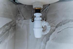 This is a closeup photograph of a sink drain located in a bathroom, showcasing the intricate details and design of the plumbing fixture and its connection to the household drainage system photo