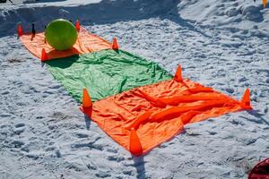 A vibrant green ball is resting on a colorful mat that features both green and orange colors, situated on the sandy beach, creating a picturesque scene of relaxation and leisure photo