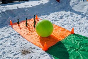 A vibrant green ball is comfortably sitting on top of a colorful orange and green tarp that is laid out in the snowy landscape all around it, creating a stunning visual contrast photo