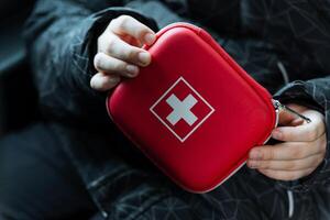 A person is confidently holding a bright red first aid kit, prominently featuring a white cross symbol, which highlights its vital role as an essential resource in medical emergencies photo