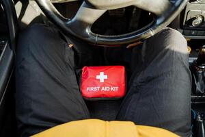 A person is seated comfortably in the drivers seat of their car, with a fully stocked first aid kit placed on their lap, prepared for any potential emergencies that may arise while driving photo