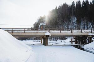 A charming bridge gracefully spans a tranquil river that is elegantly dusted with pristine white snow, showcasing natures icy beauty during the serene and peaceful winter season photo