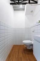 The bathroom features pristine white tiles on the walls and floor, with essential fixtures like a welldesigned toilet and sink for improved user convenience and functionality photo
