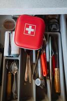 A bright red first aid kit is placed among various kinds of kitchen utensils in a drawer, emphasizing the essential importance of maintaining safety and preparedness in any home environment photo