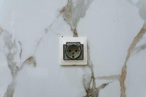 There is a white electrical outlet installed on a beautiful marble wall, accentuating the elegant design of the space. This outlet is compatible with various AC power plugs and sockets photo