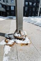 In an urban setting, there is a rusty base of a metal pole that is surrounded by a blanket of snow, showcasing a stark contrast between decay and the pristine winter landscape photo