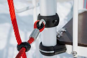 Closeup view of the playground equipment connection, featuring a rope and metal clamp attachment set against a picturesque winter scenery, highlighting its intricacies photo