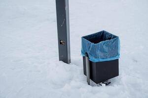 A trash bin that is completely surrounded by a thick layer of snow within a picturesque winter landscape, highlighting the contrast between trash and the serene environment photo