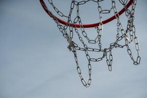 This detailed closeup image of a basketball hoop, featuring a shiny chain net contrasted against a vibrant blue sky, greatly enhances its overall visual appeal and attraction photo