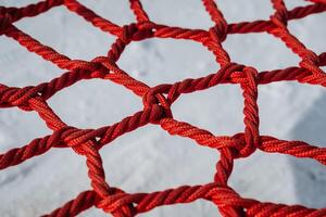 This is a closeup view of a vibrant red climbing net, complete with knots, situated on a playground surface designed for childrens adventures and safe exploration activities photo