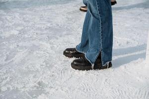 A person is standing confidently on ice, wearing stylish black boots and denim jeans, amidst a picturesque winter setting filled with snow and frost, ready for adventure photo