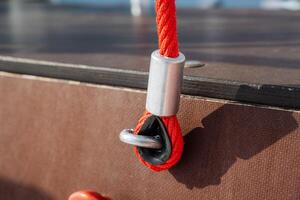 A detailed closeup image of a red rope that is firmly secured with a robust metal clamp and a hook, resting on a textured brown surface, showcasing versatility and strength photo