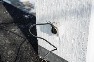 An Outdoor Electrical Outlet featuring a Plugged Power Cord mounted on a Wall, serving as a vital component for various outdoor electrical needs and functionalities photo