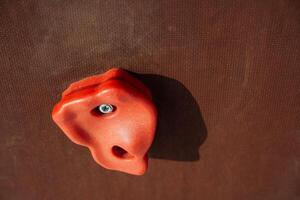 A detailed closeup view of a vibrant red climbing hold securely mounted on a sturdy brown climbing wall, specifically designed for indoor bouldering activities and practices photo