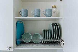 A kitchen cabinet is completely filled with various items such as plates, bowls, cups, and a cutting board, all of which are essential tools and serveware for any kitchen setup photo