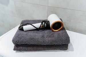 At this moment, a hair dryer is resting atop a neatly arranged stack of fluffy towels, ready to be used for personal grooming or beauty routines in a cozy bathroom setting photo