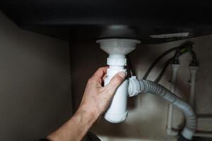 A skilled person is diligently fixing a sink pipe located under the kitchen sink, ensuring everything functions properly and adheres to plumbing standards for optimal cleanliness photo