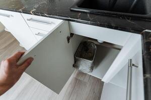 A person is in the process of opening a cabinet that is located in a kitchen, which is conveniently situated next to a sink. This activity may be part of meal preparation or organization photo